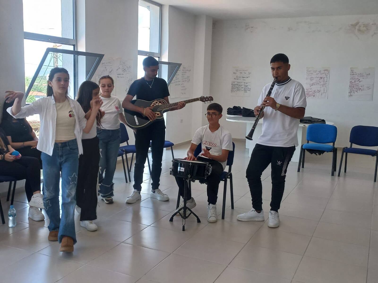 Të rinj me kitarë, klarinetë dhe daulle duke performuar në një sallë